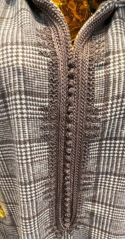 Détail du plastron d'une djellaba en lainage prince-de-galles gris&nbsp;: passementerie tressée (sfifa) et rangée de boutons cordés sphériques.