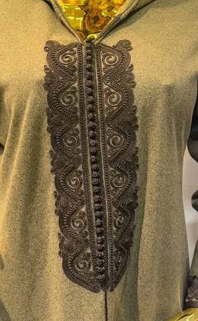 Détail du plastron d'une djellaba à capuche kaki&nbsp;: large passementerie brodée d'arabesques sombres et boutons cordés en ligne.