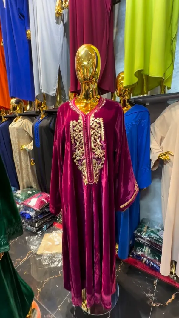 Une djellaba en velours fuchsia, plastron brodé de fil doré, sur un mannequin doré et sans visage.