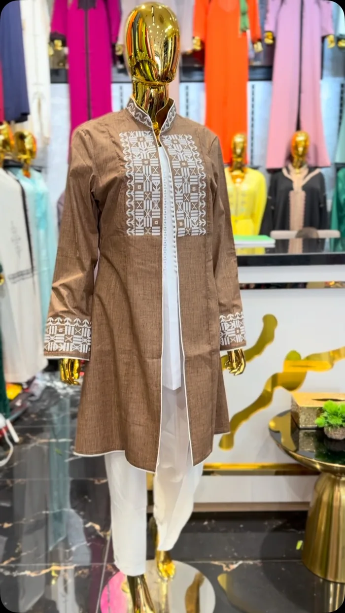Une veste ouverte, brodée sur les bords, portée sur une kurta blanche, sur un mannequin doré et sans visage.